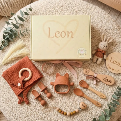 Coffret de naissance d'une douce couleur beige contenant des accessoires pour bébé, incluant des couverts, un jouet et un doudou, personnalisés avec le nom Léon.
