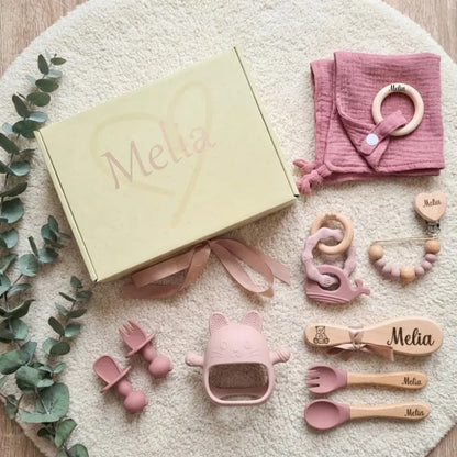  Ensemble de naissance en ton rose, comprenant des éléments pour bébé comme une sucette, des couverts et un jouet, avec le nom Mélia inscrit.