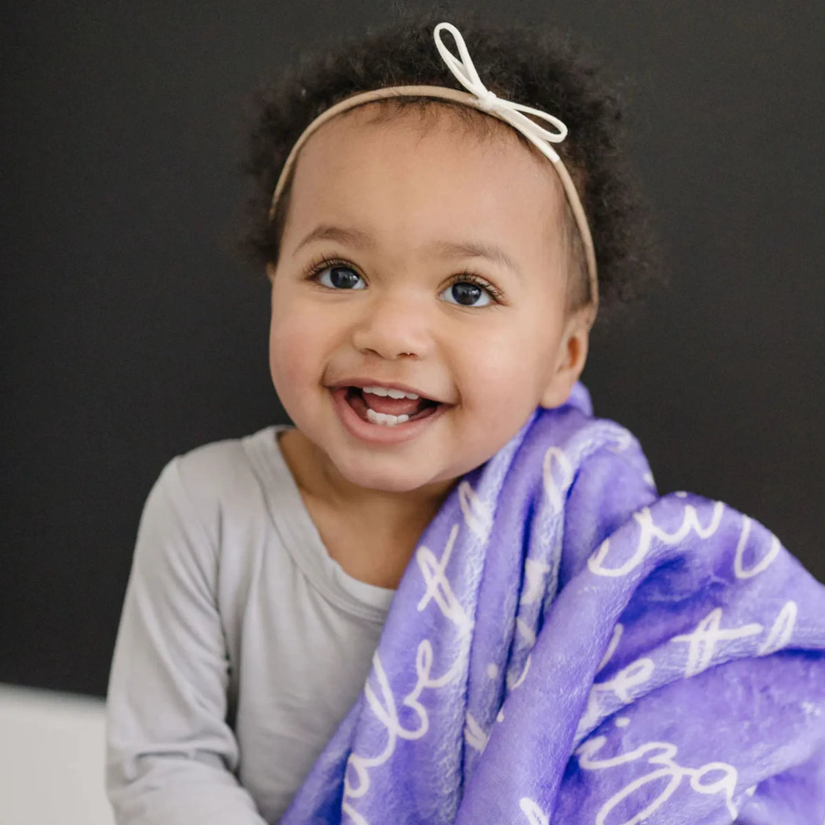 Portrait d'une très jeune fille souriante tenant un plaid personnalisé de couleur violet vibrant.