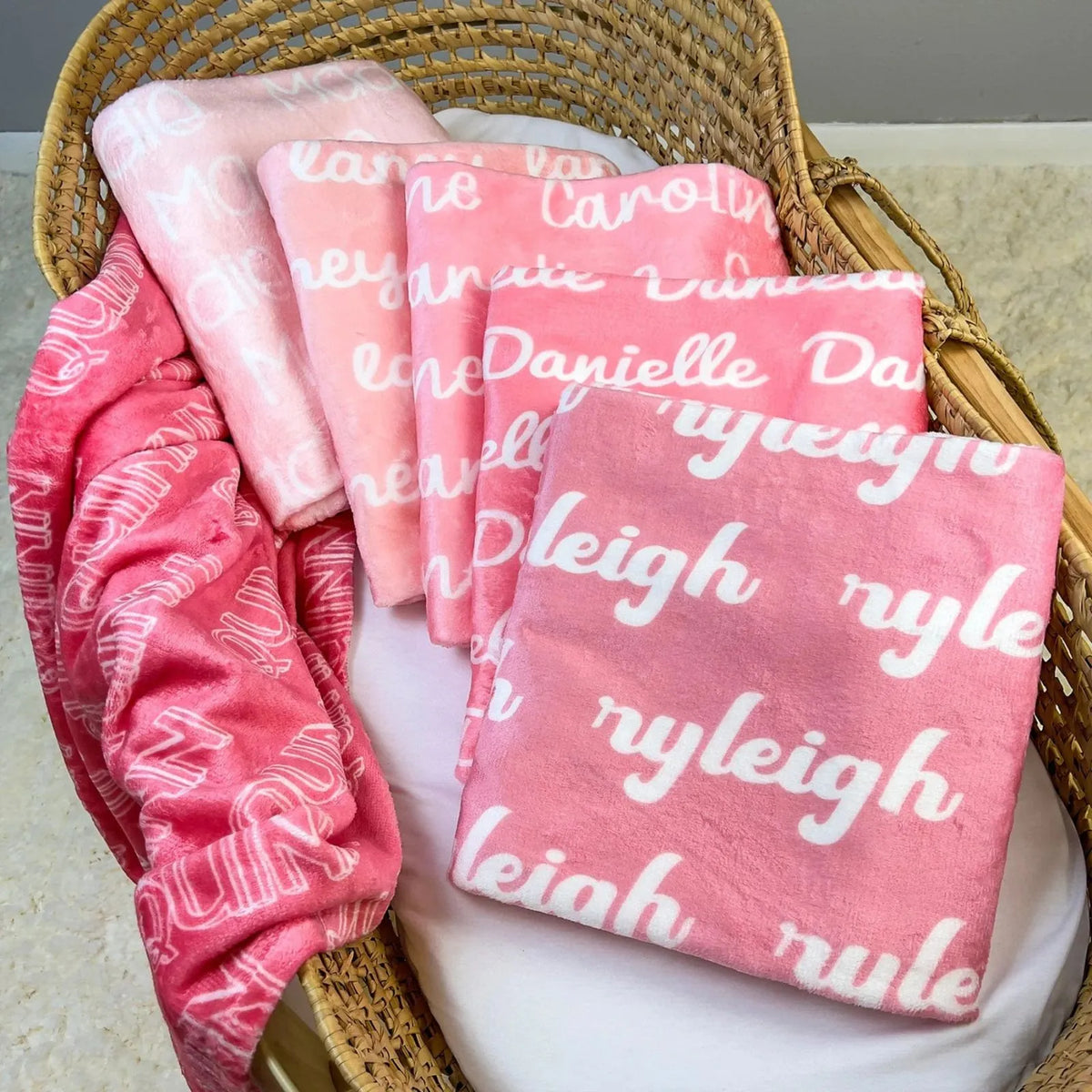 Panier cadeau naissance rempli de plaids personnalisés roses (fuchsia et pastel) avec prénoms fille. Idée présentation cadeau Baby Shower ou baptême.