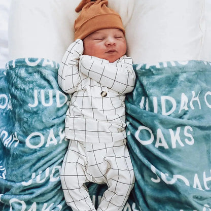Bébé stylé avec bonnet orange sur couverture personnalisée bleu canard (pétrole) prénom Judah Oaks. Accessoire de lit bébé tendance et moderne.